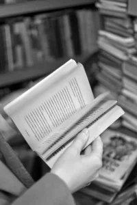 fotografía en blanco y negro de unas manos hojeando un libro en una biblioteca