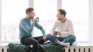 dos jóvenes hablando sentado en la repisa de una ventana