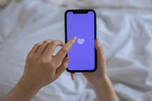 Manos utilizando una aplicaci&oacute;n de citas con un coraz&oacute;n en pantalla