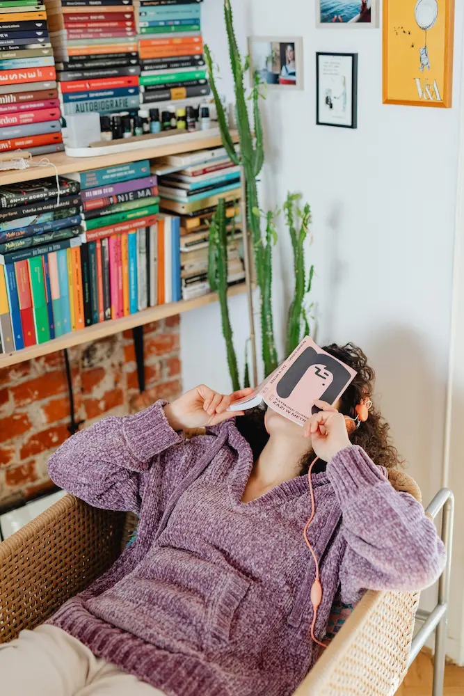 Una mujer descansando en un sillón con un libro sobre la cara frente a una estantería